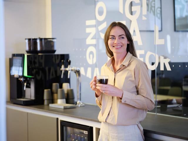 Billede af dame, der står op ad et bord og drikker en kop kaffe